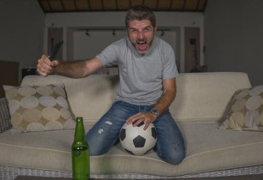 30s veya 40s futbol fan adam futbol oyunu izlerken takım gol deli mutlu çığlık tezahürat tezahürat ev oturma odası kanepede gesturing oturan