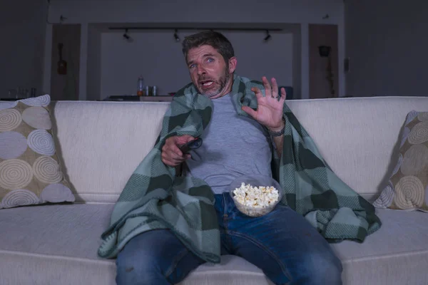 Ijedt és vicces ember egyedül éjjel a nappaliban heverő néz horror ijesztő film televíziós sikoltozik és étkezési pattogatott kukorica, amely takaró — Stock Fotó