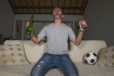30s veya 40s futbol fan adam futbol oyunu izlerken takım gol deli mutlu çığlık tezahürat tezahürat ev oturma odası kanepede gesturing oturan