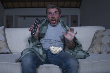 korkmuş ve komik adam yalnız gece oturma odasında kanepede televizyon çığlık korku korku filmi izlerken ve battaniye ile kaplayan patlamış mısır yeme
