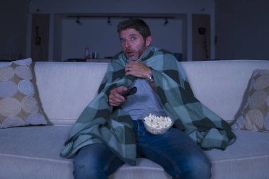 korkmuş ve komik adam yalnız gece oturma odasında kanepede korku korku filmi veya korku gösterisi izlerken televizyon battaniye ile kaplayan patlamış mısır yeme