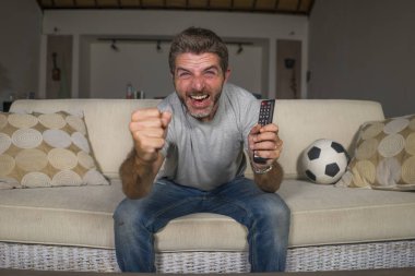 30s veya 40s futbol fan adam futbol oyunu izlerken takım gol deli mutlu çığlık tezahürat tezahürat ev oturma odası kanepede gesturing oturan