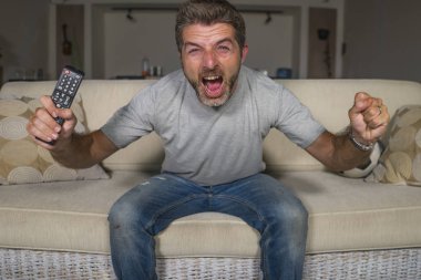 30s veya 40s futbol fan adam futbol oyunu izlerken takım gol deli mutlu çığlık tezahürat tezahürat ev oturma odası kanepede gesturing oturan