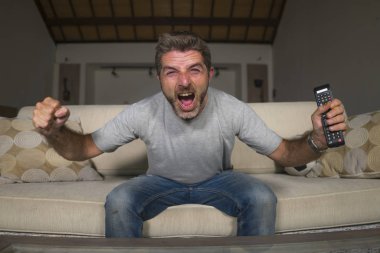 30s veya 40s futbol fan adam futbol oyunu izlerken takım gol deli mutlu çığlık tezahürat tezahürat ev oturma odası kanepede gesturing oturan