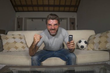 30s veya 40s futbol fan adam futbol oyunu izlerken takım gol deli mutlu çığlık tezahürat tezahürat ev oturma odası kanepede gesturing oturan