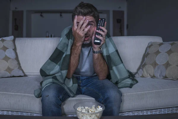 Uomo spaventato e divertente da solo di notte nel divano del salotto a guardare film horror spaventoso o spettacolo spaventoso in televisione mangiare popcorn che si coprono il viso — Foto Stock