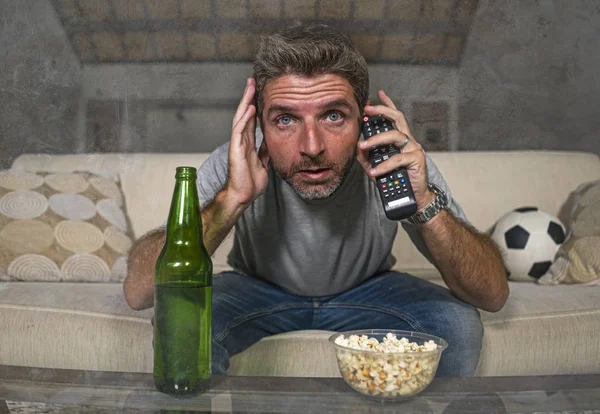 Vonzó ideg-és izgatott foci támogatója az ember néz foci játék a televízióban otthon kanapé kanapé a stressz és az érzelmek étkezési pattogatott kukorica és iszik sört — Stock Fotó