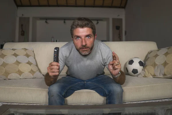 Atraente nervoso e animado torcedor de futebol homem assistindo jogo de futebol na televisão no sofá da sala de estar sentindo intensa emoção e estresse cruzando os dedos — Fotografia de Stock