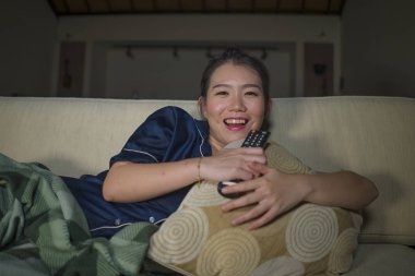 genç güzel mutlu ve neşeli Asyalı Koreli kadın Tv komedi filmi veya komik göstermek gülerek ve battaniye ile evde kanepede oturan patlamış mısır yeme izlerken 