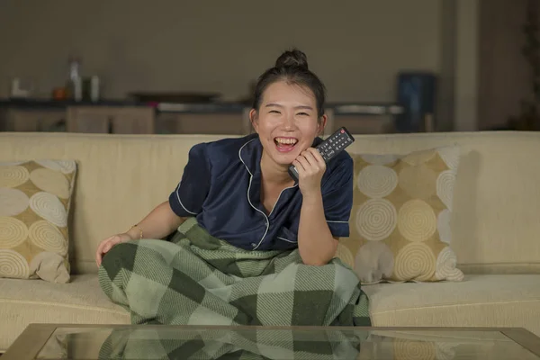 Jeune belle heureux et joyeux asiatique coréen femme regarder la télévision comédie film ou hilarant spectacle rire et manger pop-corn assis à la maison canapé avec couverture — Photo