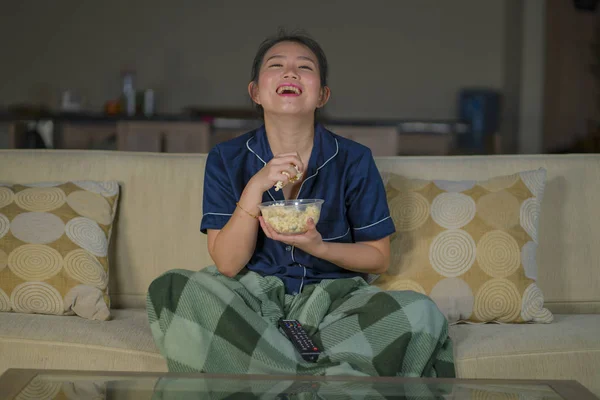 Jeune belle heureux et joyeux asiatique coréen femme regarder la télévision comédie film ou hilarant spectacle rire et manger pop-corn assis à la maison canapé avec couverture — Photo