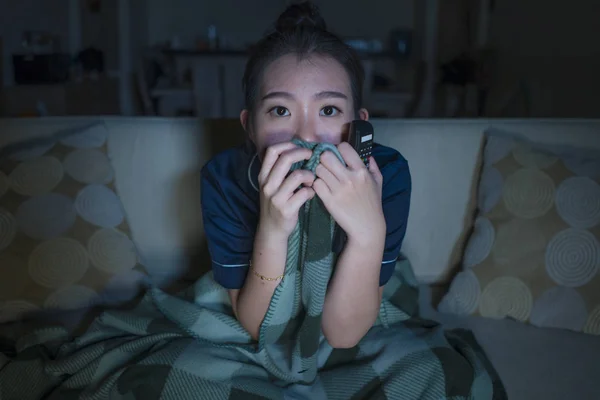 Jeune belle effrayée et effrayée asiatique femme chinoise regarder film d'horreur ou thriller manger pop-corn dans la peur expression du visage manger pop-corn sur le canapé — Photo