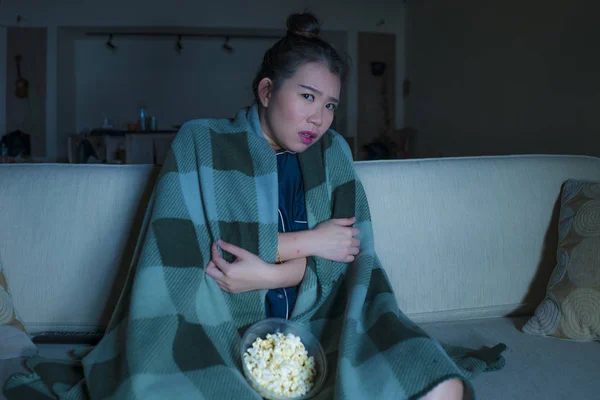 Jeune belle heureuse et joyeuse asiatique Japonais femme regarder la télévision comédie film ou hilarant spectacle rire et manger pop-corn assis à la maison canapé avec couverture — Photo