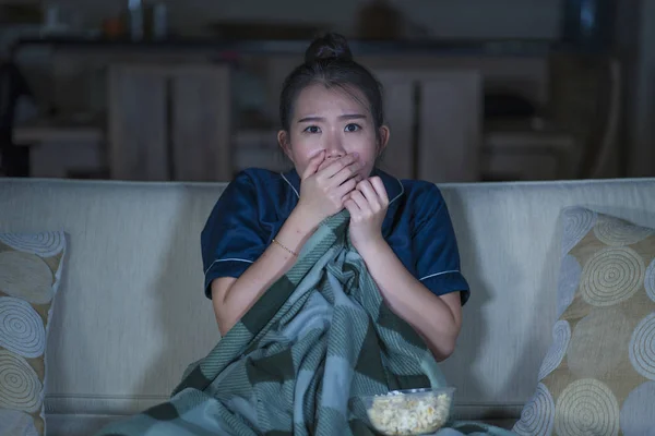 Jeune belle effrayée et effrayée asiatique femme chinoise regarder film d'horreur ou thriller manger pop-corn dans la peur expression du visage manger pop-corn sur le canapé — Photo