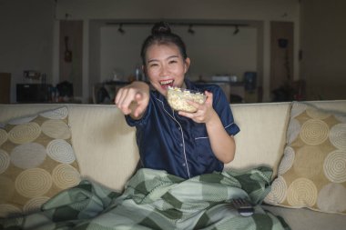 genç güzel mutlu ve neşeli Asyalı Japon kadın Tv komedi filmi veya komik göstermek gülerek ve battaniye ile evde kanepede oturan patlamış mısır yeme izlerken