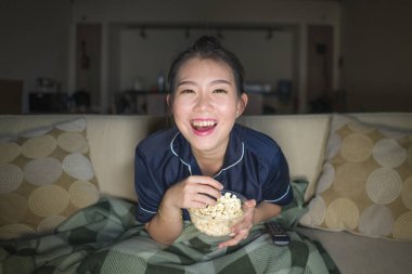 genç güzel mutlu ve neşeli Asyalı Çinli kadın Tv komedi filmi veya komik göstermek gülerek izlerken ve battaniye ile evde kanepede oturan patlamış mısır yeme 