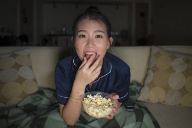 genç güzel mutlu ve neşeli Asyalı Çinli kadın Tv komedi filmi veya komik göstermek gülerek izlerken ve battaniye ile evde kanepede oturan patlamış mısır yeme 