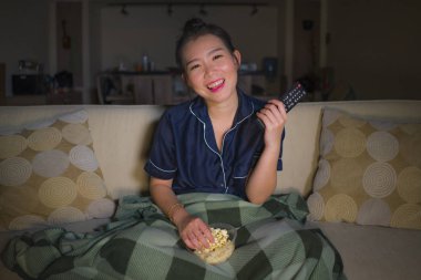 genç güzel mutlu ve rahat Asyalı Japon kadın evde oturma odasında kanepede rahat oturan Tv show bölüm veya romantik komedi filmi tatlı gülümseyen izlerken