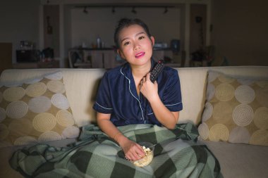 evde genç güzel mutlu ve rahat Asyalı Koreli kadın kanepede rahat oturan tv gösterisi bölüm veya romantik komedi filmi patlamış mısır yeme izlerken