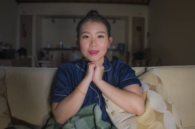 genç güzel mutlu ve rahat Asyalı Japon kadın evde oturma odasında kanepede rahat oturan Tv show bölüm veya romantik komedi filmi tatlı gülümseyen izlerken