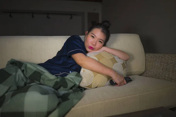 Mladá krásná šťastná a uvolněná Asijská Japonská žena v obývacím pokoji, kde sedí útulně na pohovce a dívá se na televizní seriál nebo romantický komediální film s úsměvem sladkého — Stock fotografie