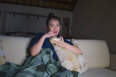evde genç güzel mutlu ve rahat Asyalı Koreli kadın kanepede rahat oturan tv gösterisi bölüm veya romantik komedi filmi patlamış mısır yeme izlerken