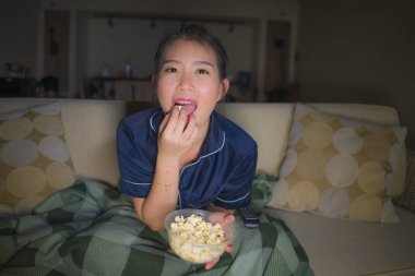 evde genç güzel mutlu ve rahat Asyalı Japon kadın kanepede rahat oturan tv gösterisi bölüm veya romantik komedi filmi patlamış mısır yeme izlerken