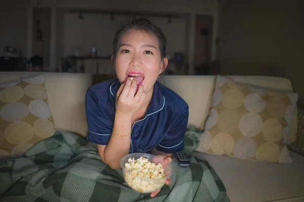 Jeune belle heureuse et détendue asiatique Japonais femme à la maison salon assis confortable sur canapé regarder la série télévisée épisode ou romantique comédie film manger pop-corn — Photo