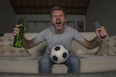 30s veya 40s futbol fan adam futbol oyunu izlerken takım gol deli mutlu çığlık tezahürat tezahürat ev oturma odası kanepede gesturing oturan