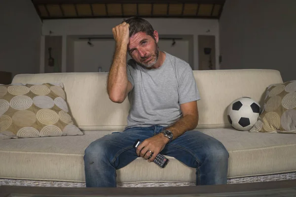 young sad and frustrated soccer fan man watching football game on television at living room couch frustrated and desperate because his team losing the game