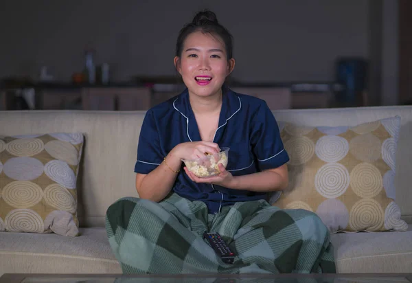 Молодая красивая счастливая и расслабленная азиатская кореянка дома сидит уютно на диване и смотрит сериал или романтический комедийный фильм улыбается сладко — стоковое фото