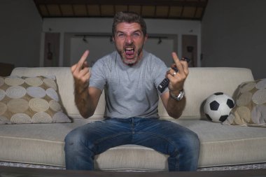 genç çılgın futbol fan adam oturma odası kanepede televizyonda futbol oyunu izlerken rakip takım alay orta parmak vererek gol kutluyor