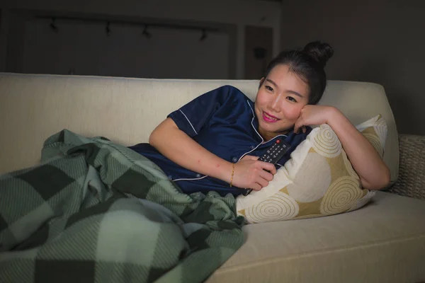 Молодая красивая счастливая и расслабленная азиатская кореянка дома сидит уютно на диване и смотрит сериал или романтический комедийный фильм улыбается сладко — стоковое фото