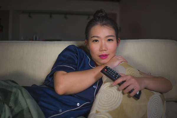 young beautiful happy and relaxed Asian Korean woman at home living room sitting cozy on sofa couch watching TV show episode or romantic comedy movie smiling sweet