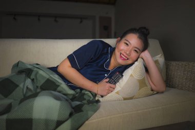 genç güzel mutlu ve rahat Asyalı Çinli kadın evde oturma odasında kanepede rahat oturan Tv show bölüm veya romantik komedi filmi tatlı gülümseyen izlerken