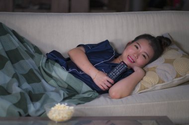 evde genç güzel mutlu ve rahat Asyalı Çinli kadın kanepede rahat yatan tv gösterisi bölüm veya romantik komedi filmi patlamış mısır yeme izlerken