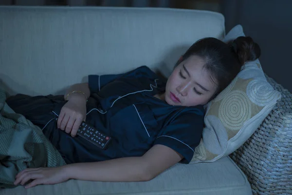 Jovem bonita e cansada mulher coreana asiática em pijama segurando TV remoto adormecer no sofá da sala de estar enquanto assiste programa de televisão ou filme à noite — Fotografia de Stock