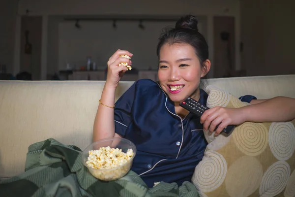 Jeune belle heureuse et détendue asiatique chinois femme à la maison salon assis confortable sur canapé regarder la série télévisée épisode ou romantique comédie film manger pop-corn — Photo