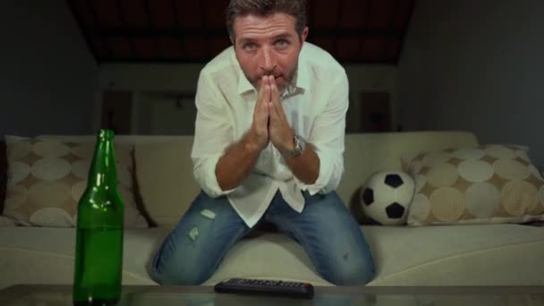 年轻迷人的兴奋的足球迷男子紧张在家里沙发上用啤酒看足球比赛庆祝进球疯狂快乐跳舞和手势在客厅沙发上感受胜利的情绪 — 图库视频影像