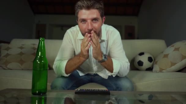 若い魅力的な興奮とストレスサッカーファンの男は 競争のストレスと感情を感じるリビングルームのソファでテレビサッカーの試合を見てビール瓶で神経質なサッカーファンの男 — ストック動画