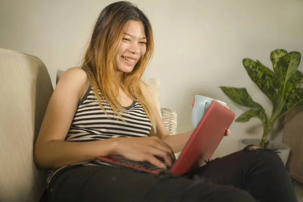 Fiatal vonzó és gyönyörű ázsiai indonéz nő otthon dolgozik nyugodt és boldog laptop számítógép nevetve a szociális média ül a nappaliban — Stock Fotó