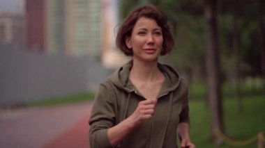 Açık havada yavaş hareket gimbal çekim takip yavaş hareket genç çekici ve uygun Kadın hoodie yeşil şehir park sabah jogging sağlıklı egzersiz çalışan 