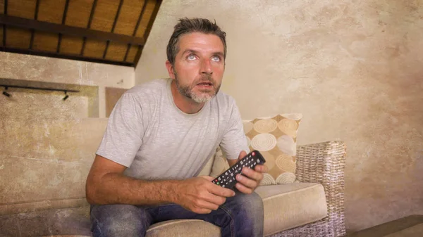 Jeune homme nerveux et excité attrayant assis à la maison salon canapé tenant la télévision à distance regarder match de football ou film d'attente dans l'expression du visage intense — Photo