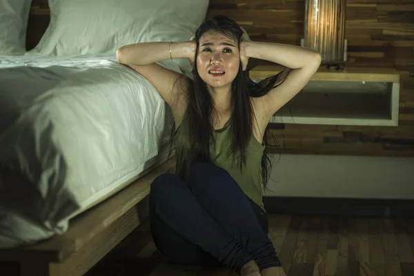 Молодая депрессивная и грустная азиатская кореянка, сидящая на полу в спальне рядом с кроватью, страдает депрессией и тревожным кризисом — стоковое фото