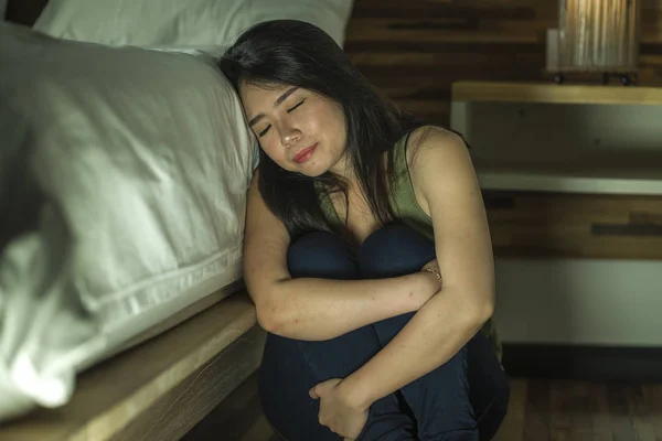 Dramatisches Lebensstil-Porträt einer jungen depressiven und traurigen asiatischen Chinesin, die im Schlafzimmer neben dem Bett auf dem Boden sitzt und unter Depressionen und Angstzuständen leidet — Stockfoto