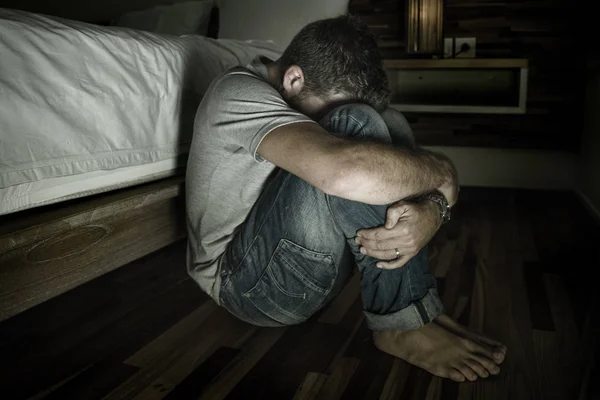 Dramatisches Porträt eines jungen verzweifelten und depressiven einsamen Mannes, der auf dem Schlafzimmerboden sitzt und weint, während er unter Angstkrise und Depressionsproblemen leidet und sich hilflos fühlt — Stockfoto