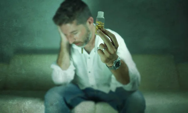 Dramatic portrait of young attractive depressed and wasted pills addict man holding antidepressant tablets bottle sitting on couch in drug addiction concept — Stock Photo, Image