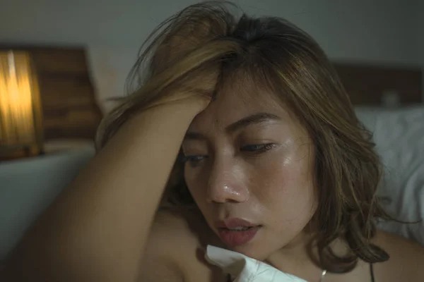 Wanita muda Indonesia yang sedih dan tertekan mengenakan gaun tidur di lantai kamar tidur dengan perasaan patah hati dan kehilangan depresi dan kecemasan — Stok Foto