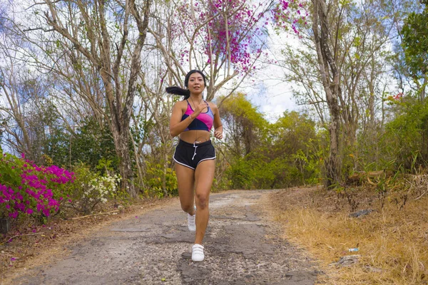 young attractive and exotic Asian Indonesian runner woman in jogging workout outdoors at countryside road track nature running sweaty pushing hard