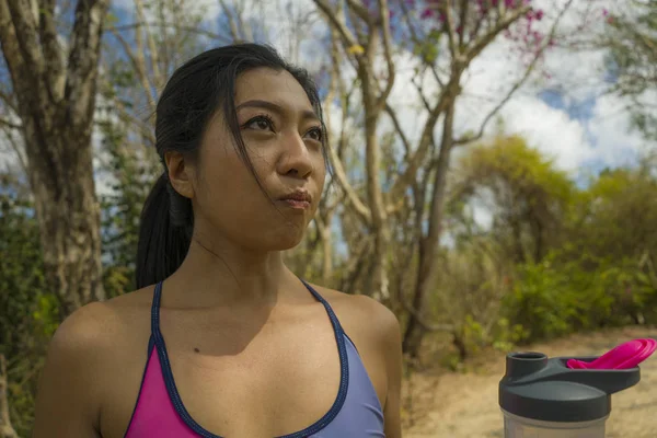 All'aperto stile di vita ritratto di giovane attraente stanca e assetata donna asiatica che beve acqua dopo duro allenamento in esecuzione raffreddamento fuori al bellissimo parco verde — Foto Stock